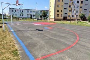 Boisko do koszykówki ulicznej na os. Piastowskim, asfaltowa nawierzchnia, kolorowe linie i grafiki oraz kosz, w tle bloki mieszkalne (photo)